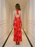 Back view of a woman in a long red halter neck dress with a tropical leaf print, standing in a hallway.
