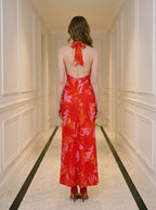Back view of a woman in a long red halter neck dress with a tropical leaf print, standing in a hallway.