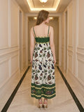 Rear view of a woman wearing a white midi dress with a green smocked bodice and a colorful bird and floral print, standing in a hallway.