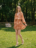 Woman wearing a floral print mini dress with long sleeves and a tie-neck standing in a grassy field