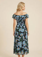 Back view of a woman in a black floral print off-the-shoulder midi dress with blue flowers and ruffle trim