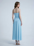 Back view of a woman in a sky blue strapless ruched jersey knit A-line evening dress with an asymmetrical hemline and side slit