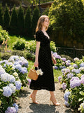 Woman walking in a garden wearing a black floral burnout velvet midi dress with puff sleeves.