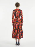 Back view of a woman in a navy blue long-sleeved midi dress with a red and yellow floral print, showcasing the tiered skirt and wrap silhouette.