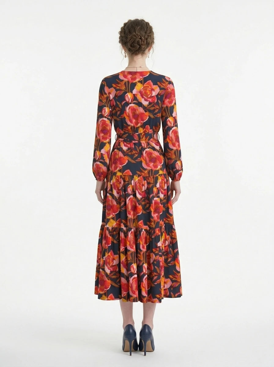 Back view of a woman in a navy blue long-sleeved midi dress with a red and yellow floral print, showcasing the tiered skirt and wrap silhouette.
