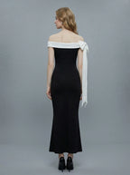 Rear view of a woman in a black off-the-shoulder mermaid dress with a white draped accent on the shoulder.