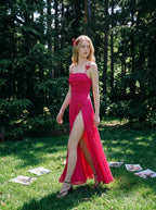 Woman in a bright pink ruched maxi dress with spaghetti straps and butterfly details, walking in a sunlit forest clearing.