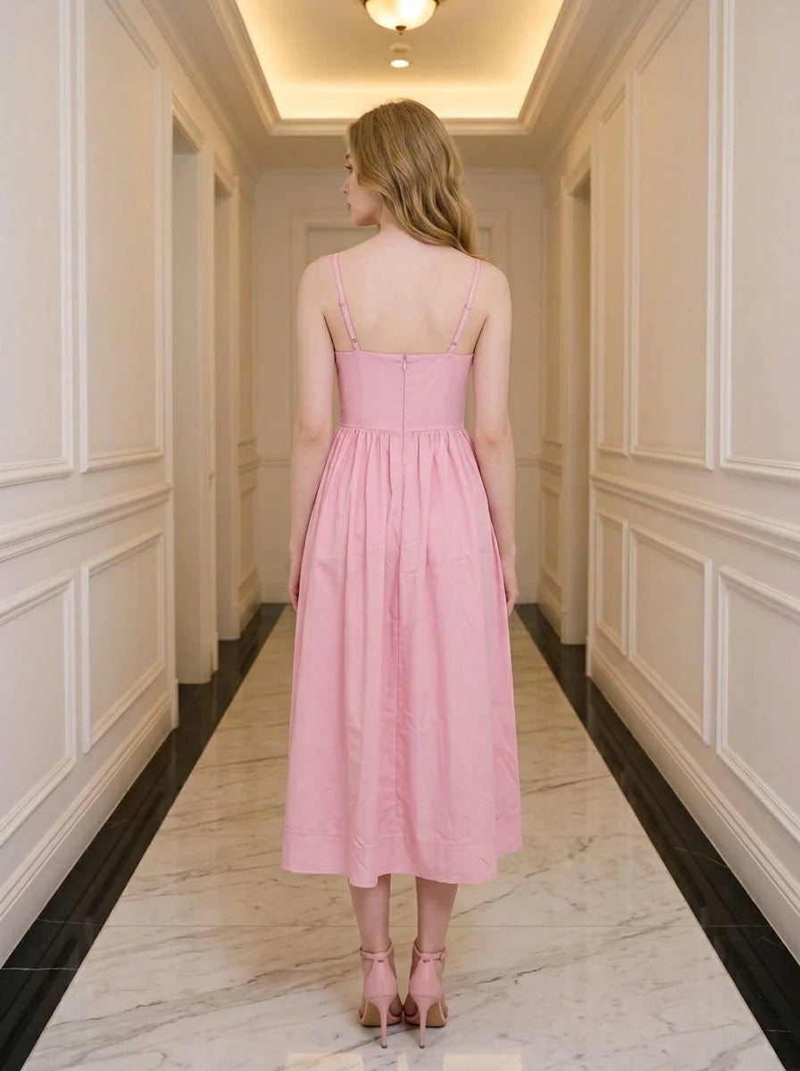 Woman wearing a pink midi dress with spaghetti straps and a square neckline, standing in a hallway.