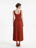 Back view of a woman in a rust-colored, sleeveless, ribbed knit maxi dress with a scoop neckline and gathered waist, standing against a white background.