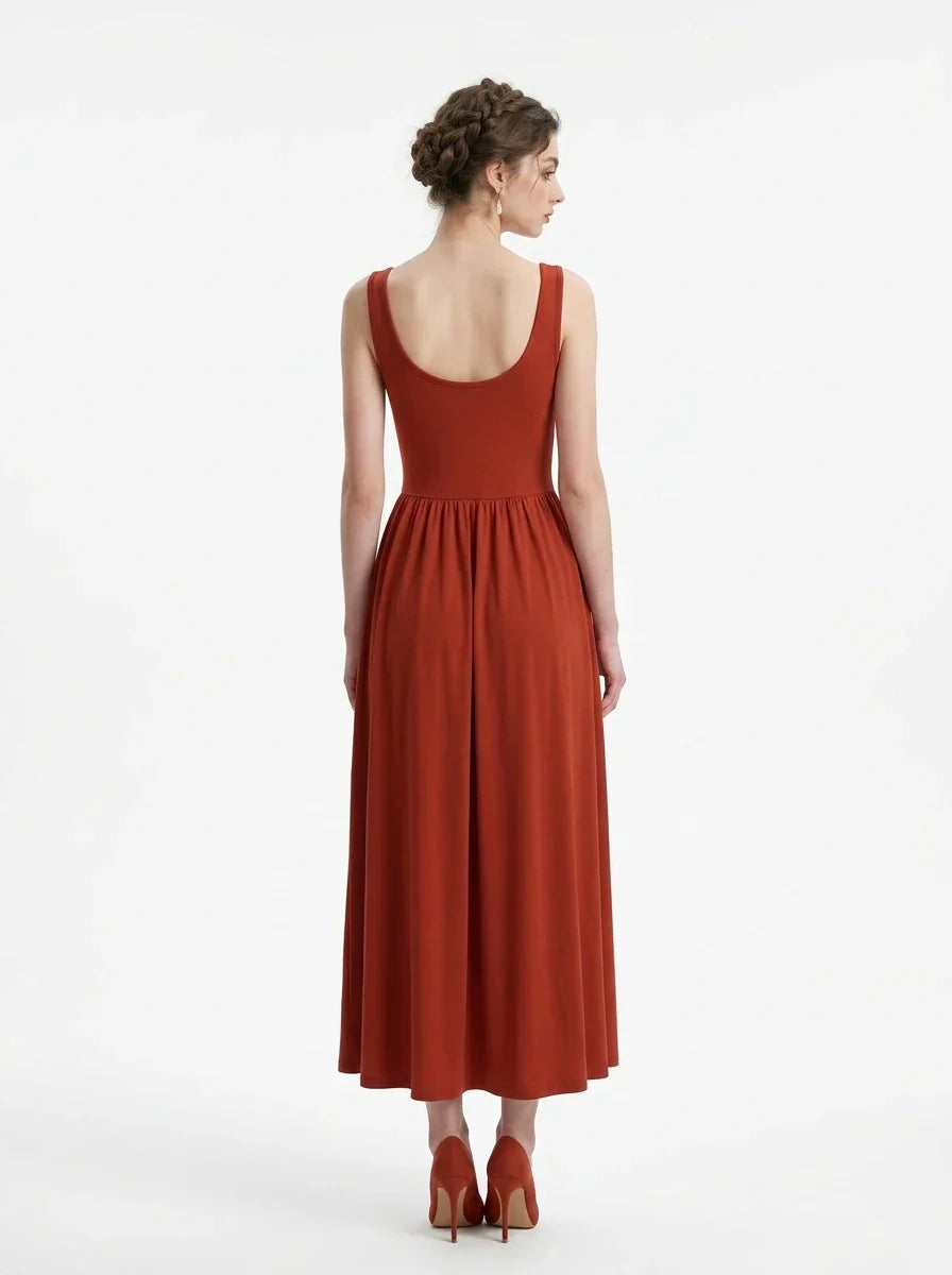Back view of a woman in a rust-colored, sleeveless, ribbed knit maxi dress with a scoop neckline and gathered waist, standing against a white background.