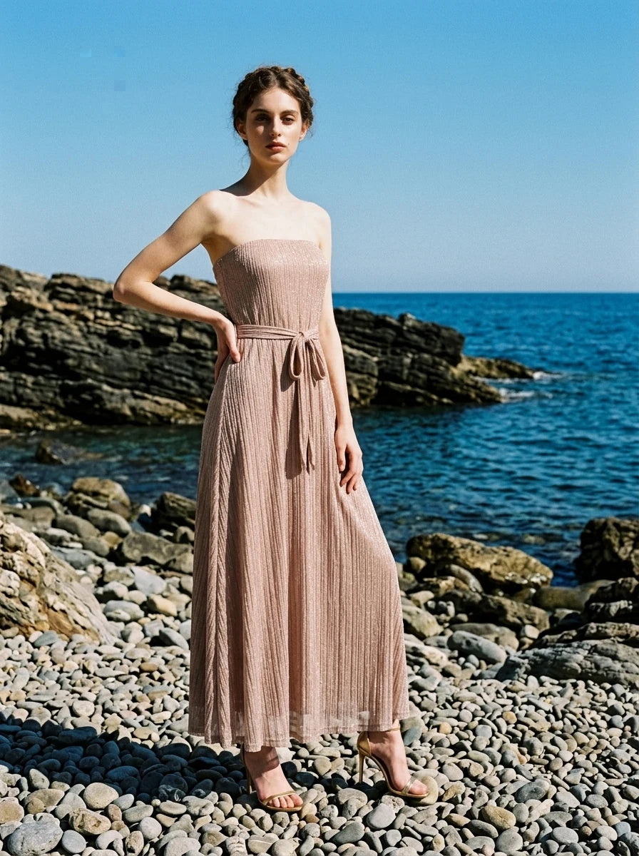 Woman wearing a strapless metallic knit A-line maxi dress with a self-tie belt on a rocky shore