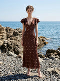 Woman in a brown polka dot midi dress with ruffled sleeves on a rocky beach.
