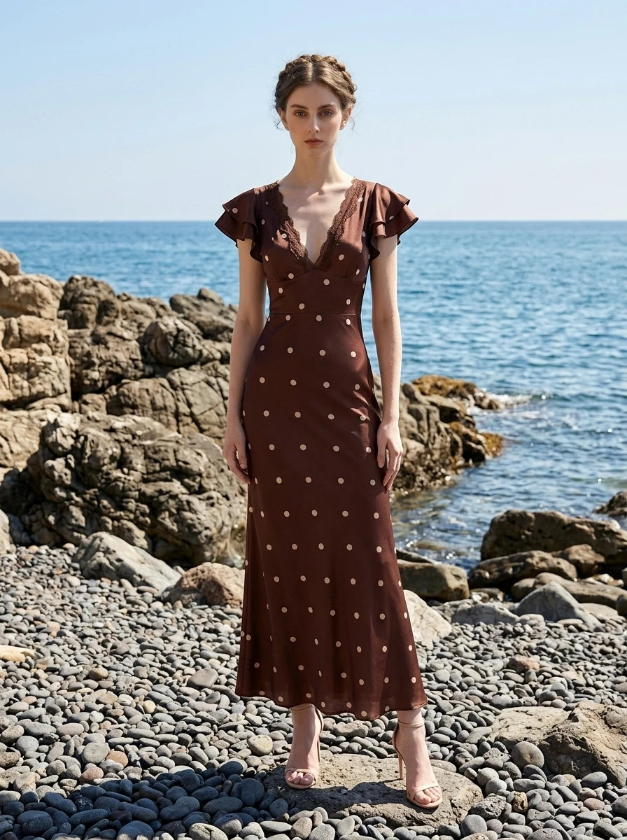 Woman in a brown polka dot midi dress with ruffled sleeves on a rocky beach.