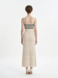 Woman wearing a cream knit maxi dress with black striped bodice and spaghetti straps, back view