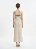 Woman wearing a cream knit maxi dress with black striped bodice and spaghetti straps, back view