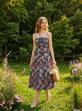 Woman wearing a navy floral print midi dress with spaghetti straps and a peplum waist, walking through a garden with pink flowers.