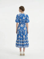 Back view of a woman in a blue floral print midi dress with puff sleeves and a tiered skirt.
