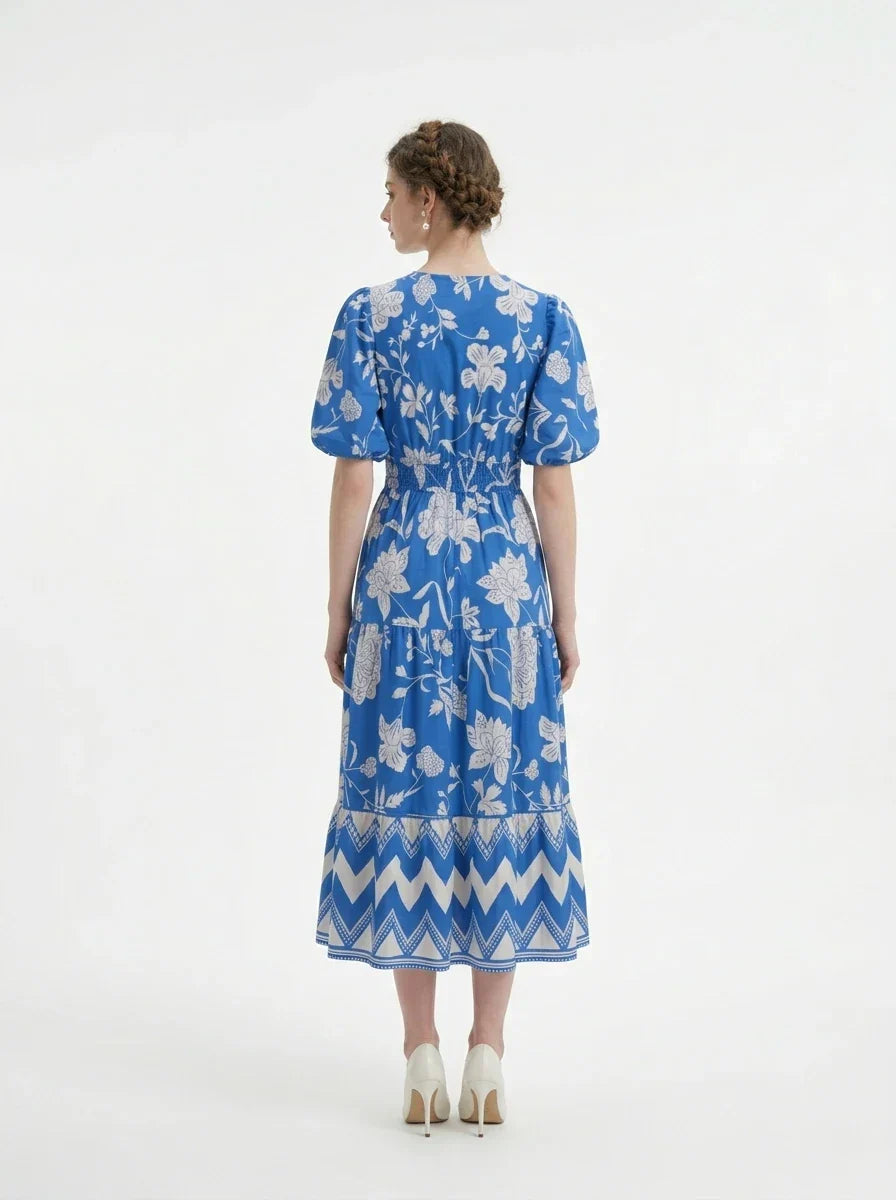 Back view of a woman in a blue floral print midi dress with puff sleeves and a tiered skirt.