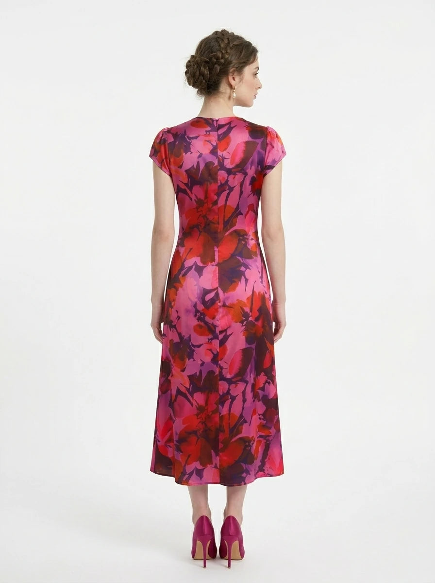 Woman in a pink and red floral print satin ruched midi dress with cap sleeves.