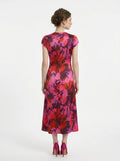 Back view of a woman in a pink and red floral print satin ruched midi dress.