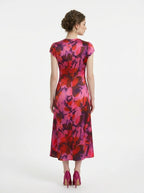 Back view of a woman in a pink and red floral print satin ruched midi dress.
