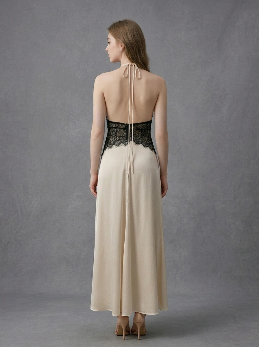 Rear view of a woman in a cream satin maxi dress with black lace detailing at the waist and a halter neckline, showing the open back and tie closure.