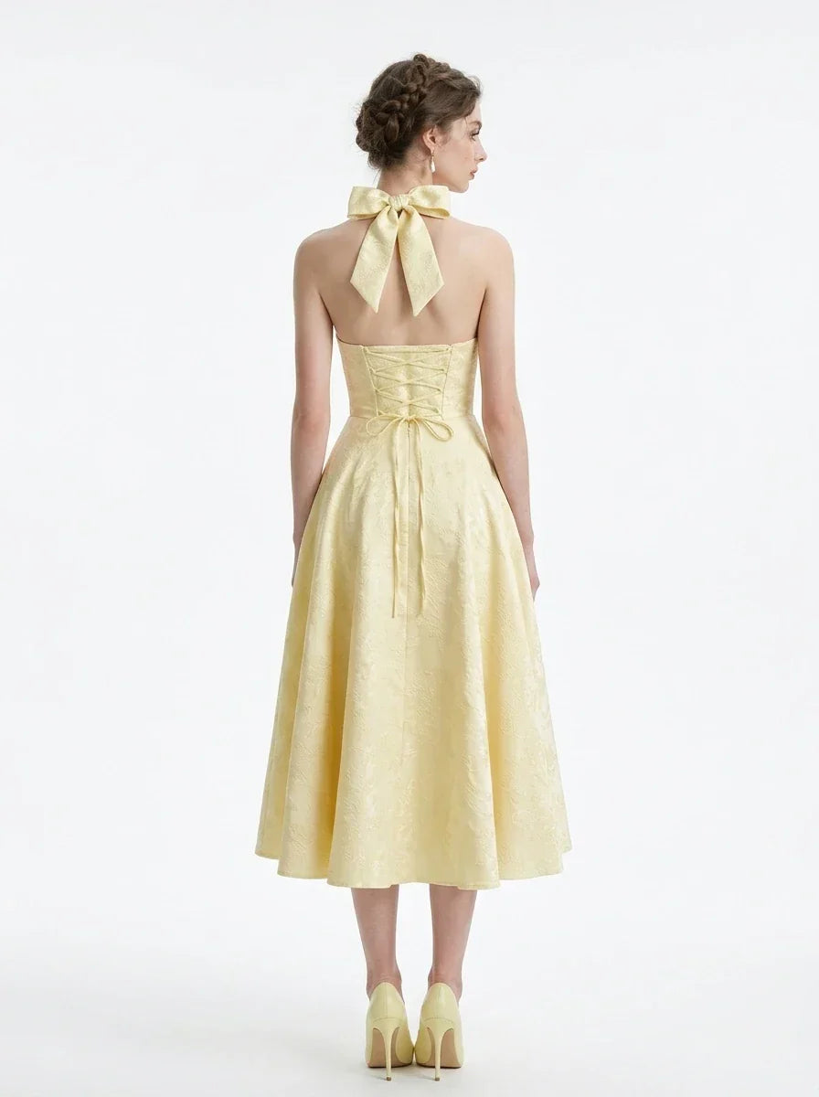 Woman wearing a pale yellow jacquard halter neck midi dress with a V-neckline and a corset back.