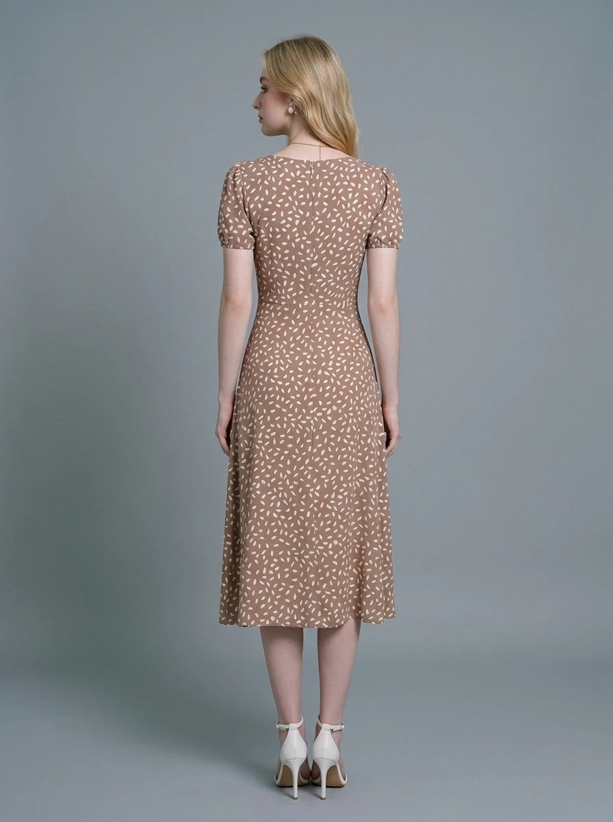 Woman wearing a brown midi dress with a white abstract print, puff sleeves, sweetheart neckline, and a high side slit.
