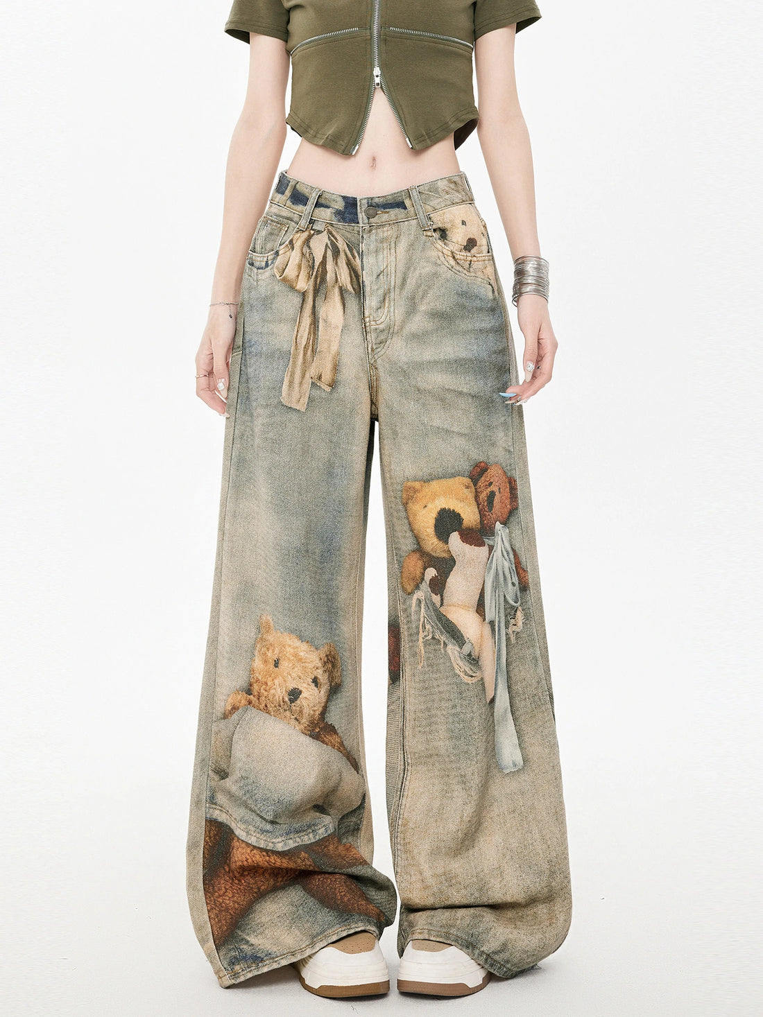 Woman wearing wide leg denim pants with teddy bear graphic print and tie waist, paired with a cropped olive green top.