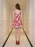 Rear view of a woman in a red and white floral print sleeveless fit and flare dress with a square neckline, standing in a hallway.