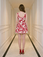 Rear view of a woman in a red and white floral print sleeveless fit and flare dress with a square neckline, standing in a hallway.