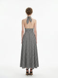 Back view of a woman in a black and white gingham check halter neck maxi dress with a plunging V-neck and a defined empire waist.