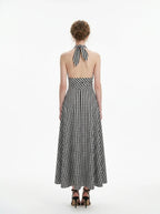 Back view of a woman in a black and white gingham check halter neck maxi dress with a plunging V-neck and a defined empire waist.