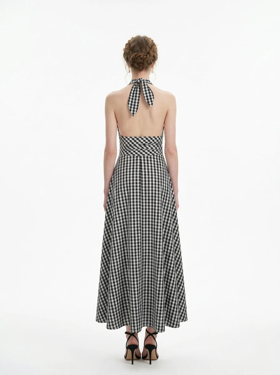 Back view of a woman in a black and white gingham check halter neck maxi dress with a plunging V-neck and a defined empire waist.