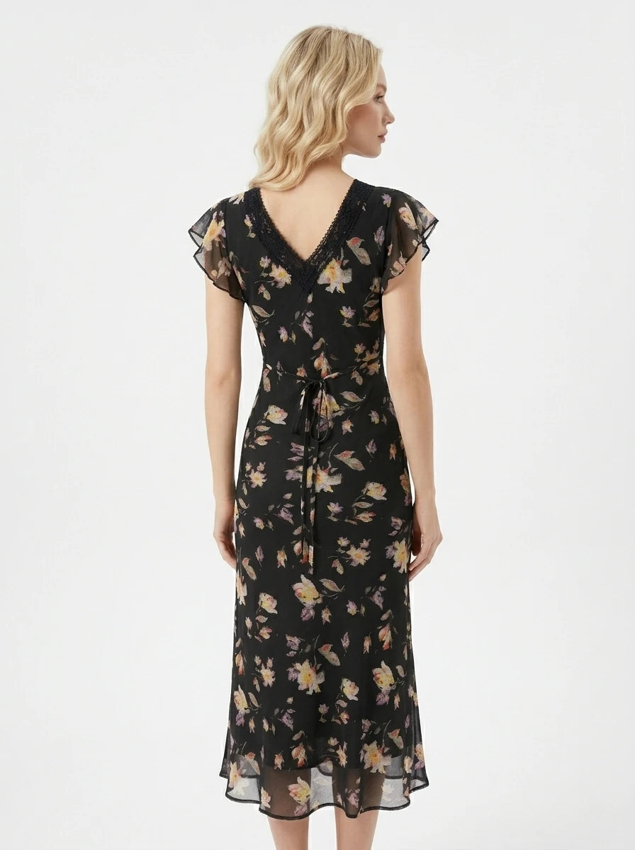 Woman wearing a black floral print midi dress with flutter sleeves and lace trim.