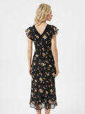 Back view of a woman in a black floral print midi dress with a tie-back waist.