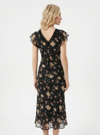 Back view of a woman in a black floral print midi dress with a tie-back waist.