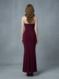 Back view of a woman in a burgundy strapless ruched maxi dress with gold waist embellishment.