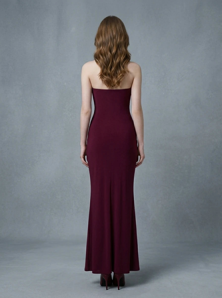 Back view of a woman in a burgundy strapless ruched maxi dress with gold waist embellishment.