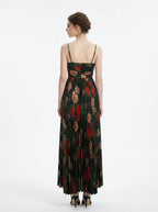 Woman in a dark green floral print maxi dress with spaghetti straps and a pleated skirt, back view