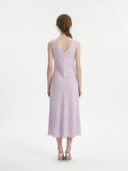 Back view of a woman in a lilac midi dress with a V-neckline and sleeveless design.