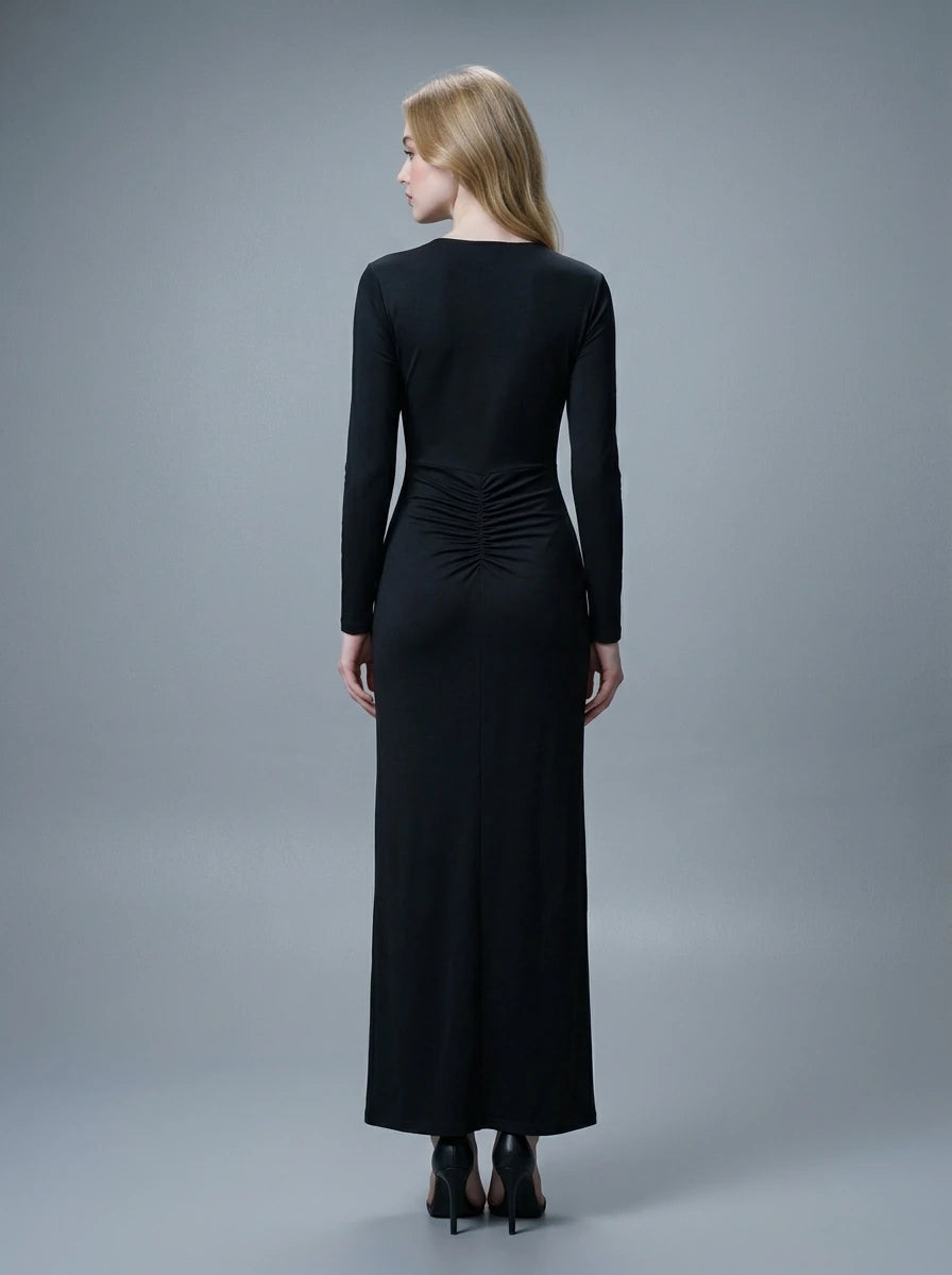 Woman in a black long-sleeved V-neck gown with a front knot and high slit, standing against a grey backdrop.