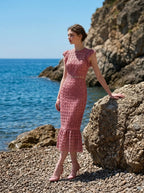 Model standing on rocks by the sea in Dusty Rose Lace Midi Dress