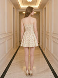 Back view of a woman in a yellow floral print mini dress with a lace-up back detail, standing in a hallway.