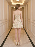 Back view of a woman in a yellow floral print mini dress with a lace-up back detail, standing in a hallway.