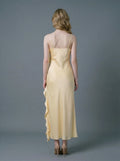 Back view of a woman in a pale yellow satin one-shoulder gown with a ruffled high slit.