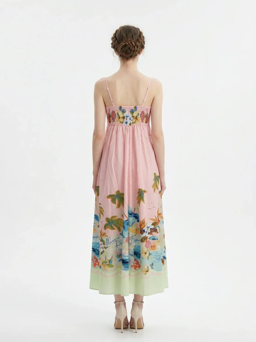 Woman wearing a pink midi dress with spaghetti straps and a tropical print of palm trees and flowers.