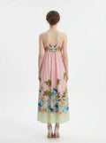 Back view of a woman in a pink midi dress with spaghetti straps and a tropical print.