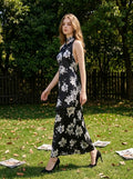 Woman walking in a grassy area wearing a black floral print halter maxi dress