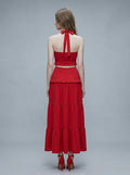 Back view of a woman in a red halter neck crop top and tiered maxi skirt.